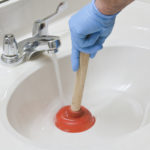 Removing a clog in the sink with a plunger.