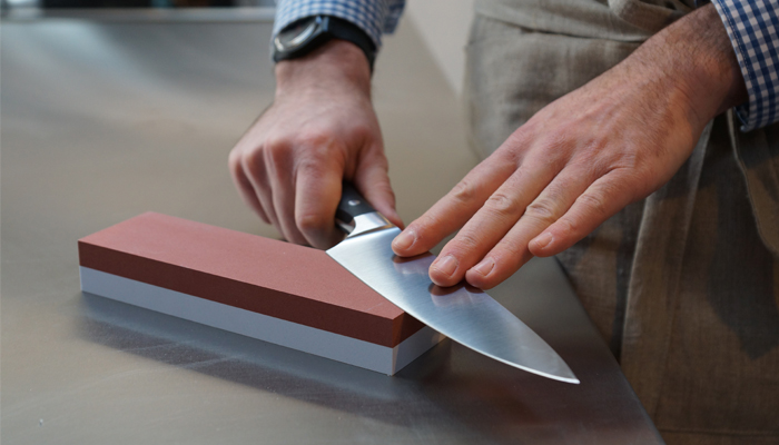 A man sharpens a knife on a whetstone